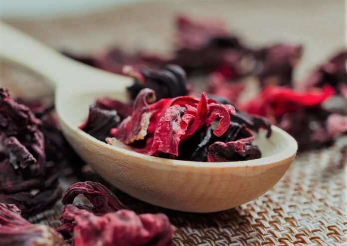 Petals of tea on a wooden spoon close-up. Macro photo of red petals of Sudanese rose, hibiscus flower. Tea composition from tea petals of the Sudanese rose located in a spoon on a natural background.